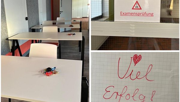 Im Bild ist ein Klassenraum mit mehreren weißen Tischen und Stühlen zu sehen, auf jedem Tisch liegt ein kleines Päckchen mit Süßigkeiten als Glücksbringer. An einer Tür hängt ein Schild mit der Aufschrift „Bitte Ruhe!!! Examensprüfung“. Auf einem weiteren Blatt steht handgeschrieben „Viel Erfolg!“ mit einem Herz und einem gezeichneten Kleeblatt.