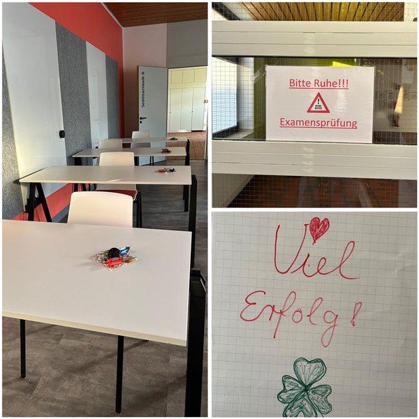 Im Bild ist ein Klassenraum mit mehreren weißen Tischen und Stühlen zu sehen, auf jedem Tisch liegt ein kleines Päckchen mit Süßigkeiten als Glücksbringer. An einer Tür hängt ein Schild mit der Aufschrift „Bitte Ruhe!!! Examensprüfung“. Auf einem weiteren Blatt steht handgeschrieben „Viel Erfolg!“ mit einem Herz und einem gezeichneten Kleeblatt.