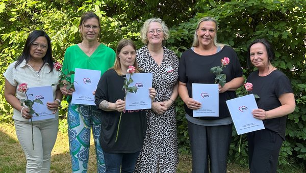 Sechs Personen stehen nebeneinander im Grünen, halten Urkunde und Rosen in den Händen und lächeln in die Kamera
