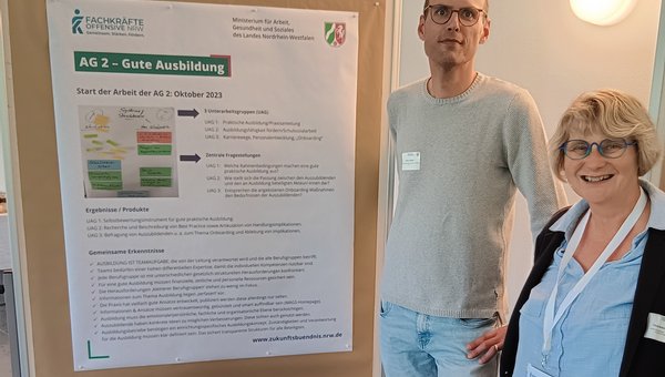Zwei Personen stehen vor einem Informationsposter mit dem Titel „AG 2 – Gute Ausbildung“. Rechts im Vordergrund befindet sich Claudia Bertels-Tillmann, neben ihr steht Torsten Jaspers. Das Poster zeigt Textinhalte zur Ausbildungsqualität.